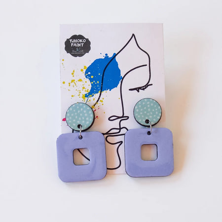 A pair of Tjhoko Paint Trish dangle earrings featuring light blue dotted round tops and lavender square drops with cutouts,