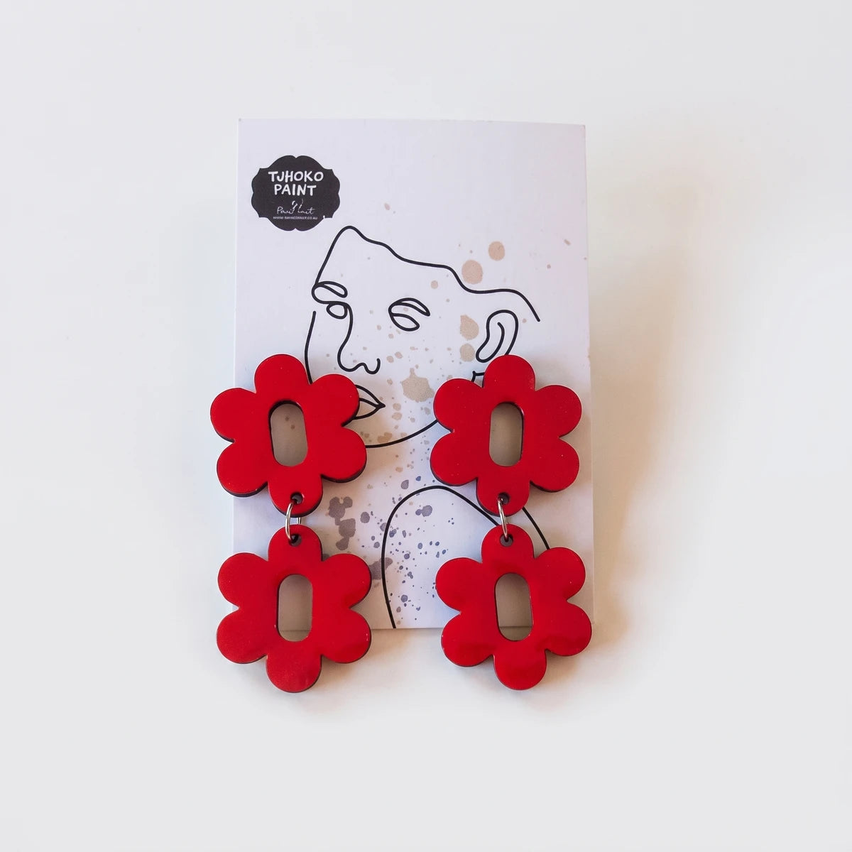 Real Red double daisy earrings from Tjhoko Paint, displayed on a white branded card against a textured background.