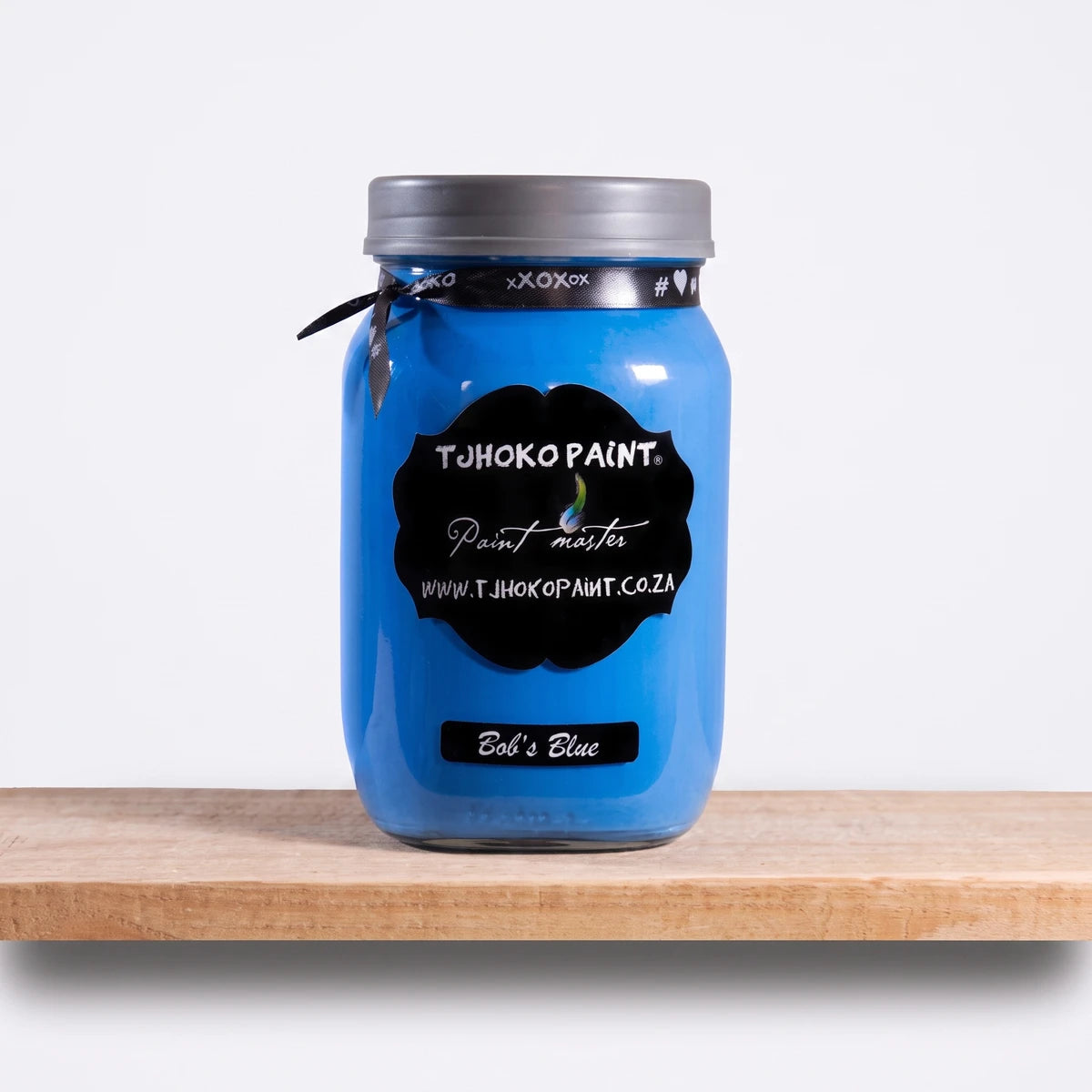 Bob's Blue 1L Chalk Paint jar from Tjohoko Paint, displayed on a natural wooden shelf in a studio setting.