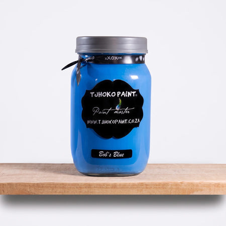 Bob's Blue 1L Chalk Paint jar from Tjohoko Paint, displayed on a natural wooden shelf in a studio setting.