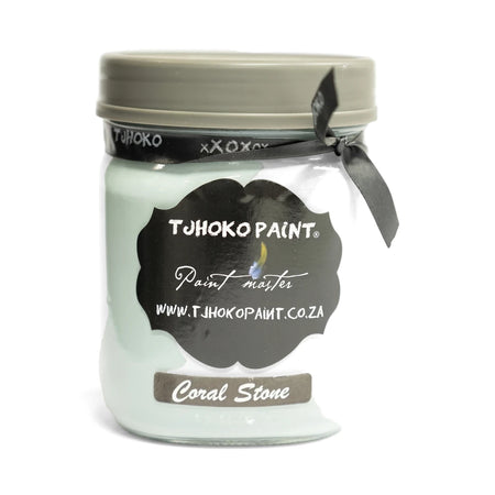 A 500ml glass jar of Tjohoko Paint in Coral Stone, a light teal color, with a gray lid and black ribbon.