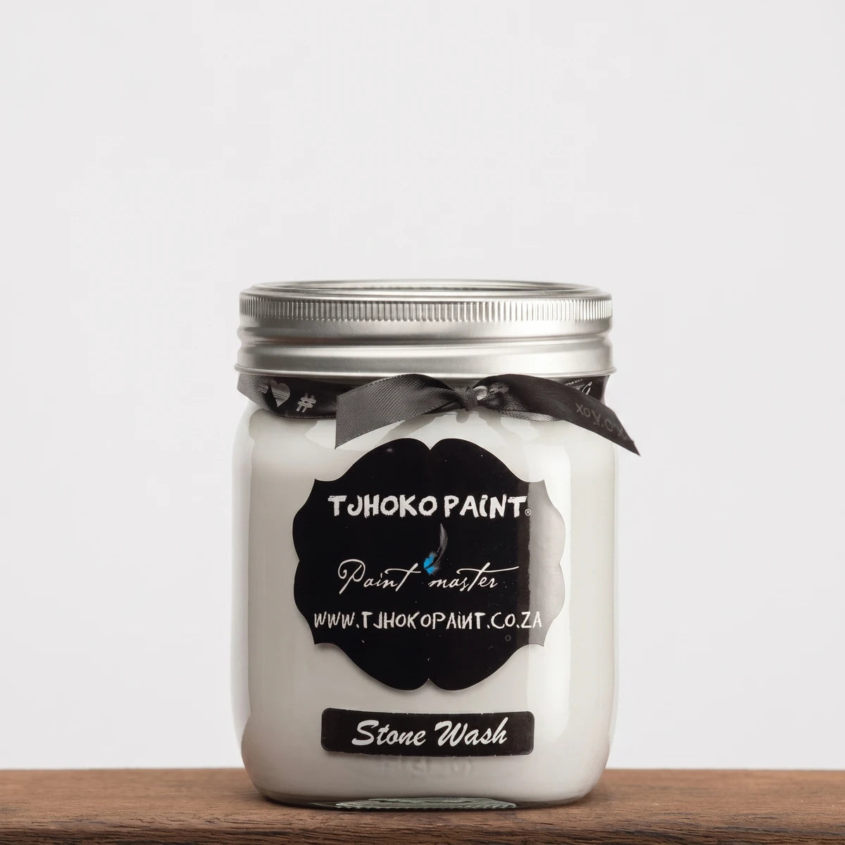 White Tjohoko Paint Stone Wash 250ml chalk paint in a glass jar with a black label and silver lid, resting on a wooden