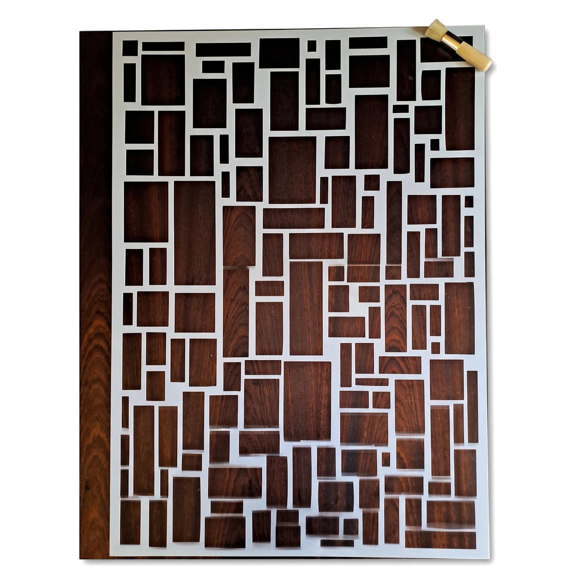 White paint stencil with a modern geometric rectangular pattern, displayed flat with a small stippling brush on a wooden