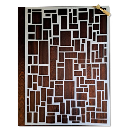 White paint stencil with a modern geometric rectangular pattern, displayed flat with a small stippling brush on a wooden
